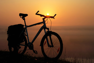 Fototapeta na wymiar Silhouette of a bicycle against the orange sky at sunrise, with sun as a headlight
