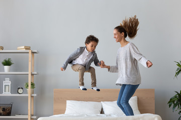 Happy mom have fun jumping with little son on bed