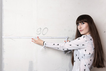Young woman holds a folding meterstick carpenter's ruler in front of a measurement on a gray wall...