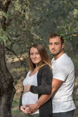 Obraz premium Pregnant couple standing next to a tree and smiling at camera