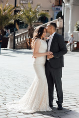 Naklejka premium Happy couple in love on the background of buildings. Love story of couple in the city. Love story. Portrait of a beautiful young couple in love standing and kissing