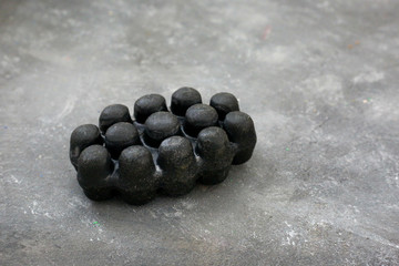 Black charcoal volcanic soap and herbal leaves on grey background.