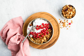 Breakfast cereal oat granola with yogurt and red currant berries on grey concrete background. Table top view. Healthy breakfast food, clean eating concept