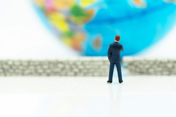 Miniature people: Businessman standing with wall and world. Concepts of finding a solution, problem...