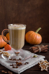 Pumpkin latte with spices and honey in a glass glass on a wooden background. Pumpkins, cookies, cinnamon, cloves and coffee. Autumn mood. Side view, copy space. Dark photo