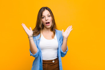 young pretty woman looking shocked and astonished, with jaw dropped in surprise when realizing...