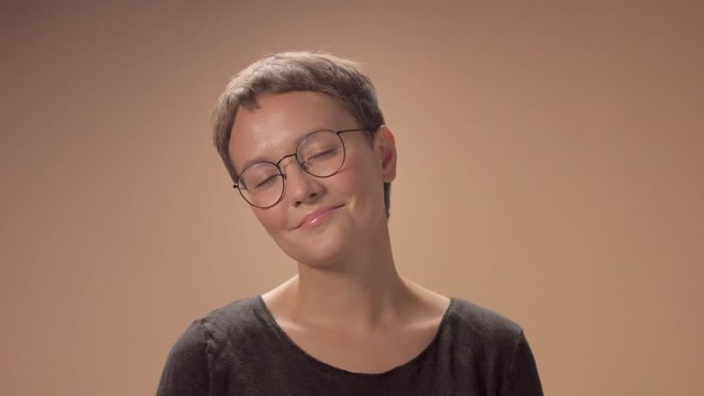 Caucasian woman with short haircut wears glasses in studio on beige background