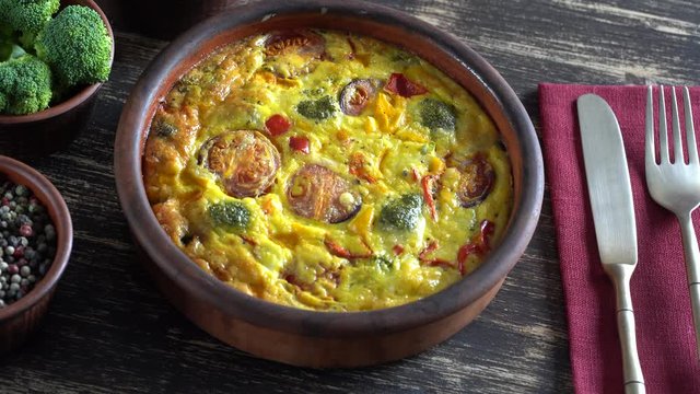 Ceramic bowl with vegetable frittata, simple vegetarian food. Frittata with egg, tomato, pepper, onion, broccoli and cheese on wooden table, close up. Italian egg omelette, rotates