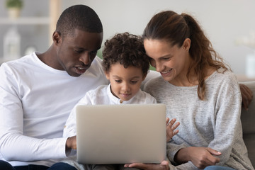 Smiling international family with kid using laptop at home