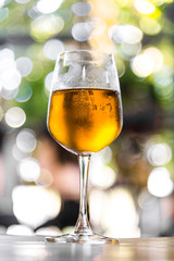 Glass of mug golden beer on wood table and green light blured bokeh garden outdoor background