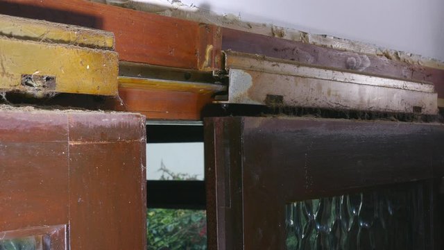 Close POV shot of the accumulated dirt, dust and cobwebs on the hanging rail, glide mechanism of two heavy wooden interior sliding doors with glass panes, being closed together.