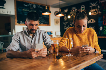 couple sitting one beside other using mobile phones.