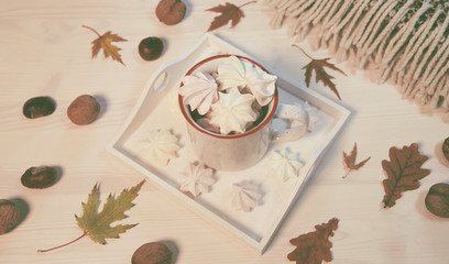 Fototapeta na wymiar Autumn composition with a cup of meringues, yellow leaves, chestnuts, walnuts and wool blanket on a white wooden background
