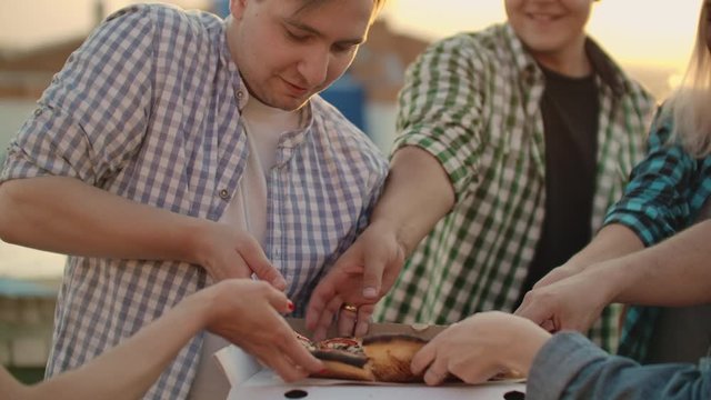 A company of six young people parses pieces of hot pizza together
