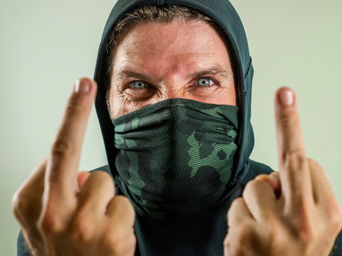 young man as fanatic and aggressive anarchist rioter giving middle finger. furious and scary violent anti-system protester in face mask screaming hostile at fighting riot