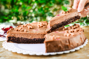 Delicious caramel cake in woman hand on white plate. Finest piece of chocolate tart and mint on top dish out...