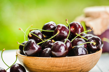 Black cherries in wooden bowl on white table. Cherry jam blurred in background.
