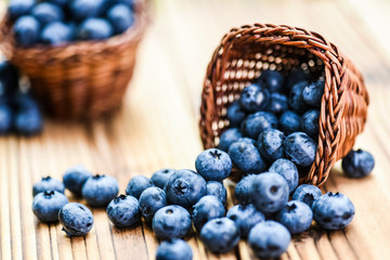 Blueberries on wooden rustic table. Wicker basket full of blueberry in background.