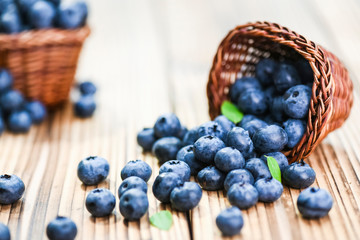 Fresh finest blueberries in small wicker basket. Few blueberry sprinkled or leaved on rustic table.