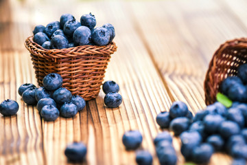 Fresh finest blueberries in small wicker basket. Few blueberry sprinkled or leaved on rustic table.