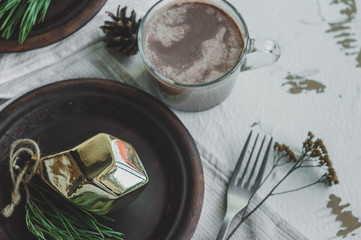 Christmas and New Year table setting in rustic style with handmade details. Dining place decorated with handmade dishes, pine cones, branches and golden christmas decorations 