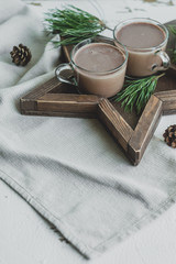 Star-shaped Wooden Tray with two cups of cocoa. Christmas decor with rustic style elements on a white background. Cones and pine branches New Year's decor.