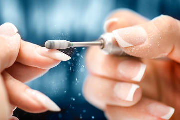 Woman use electric nail file drill in beauty salon. Perfect nails manicure process or operation in close up with burst flying debris. - obrazy, fototapety, plakaty