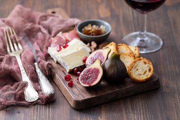 figs with cheese and pomegranate on wooden board and red wine on ceramic background