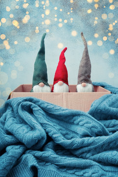 Three Christmas gnomes of different colors in open box, knitted blanket