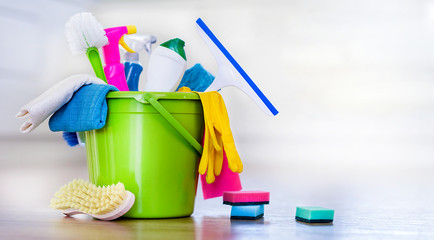 Basket or bucket with cleaning items on blurry modern kitchen background. Washing set colorful with...