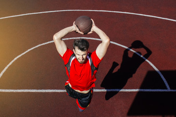 Young bearded guy athlete performs a slam dunk in a jump. Basketball player jumps and casts a shadow on the sports field. A beautiful jump and toss of a basketball into the basket. © Daniil