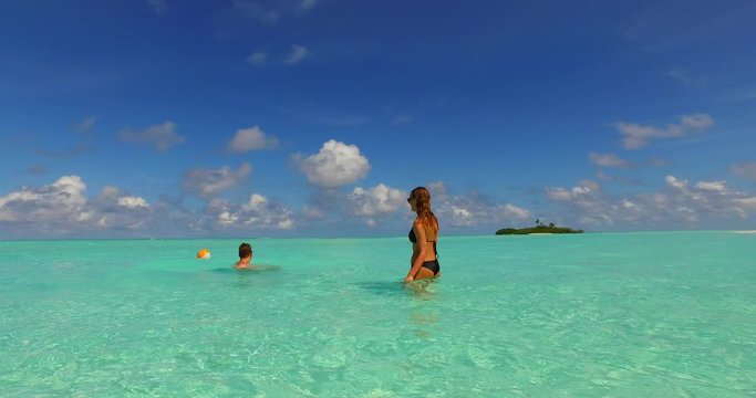 A young couple playing with an inflatable beach ball in shallow tropical water in the Caribbean