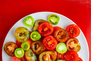 Sliced red, green and kumato tomatoes on white plate on red wooden background