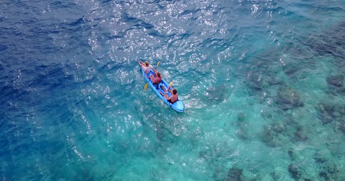 Aerial overhead view of 3 tourists kayaking in crystal clear waters of the Philippine sea. Drone corkscrew shot