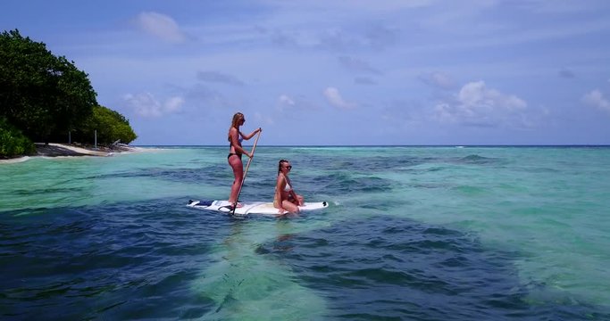 best friends having fun on the paddleboard. Girl rowing in the seawater while her friend is sunbathing. Choppy water of gulf of thailand