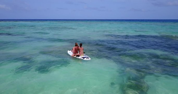 Two young ladies in the bikinis paddling on the baddleboard on the crystal clear gulf of thailand