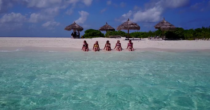 group of 5 beautiful women in bikinis sunbathing and chatting on white sand beach, jamaica