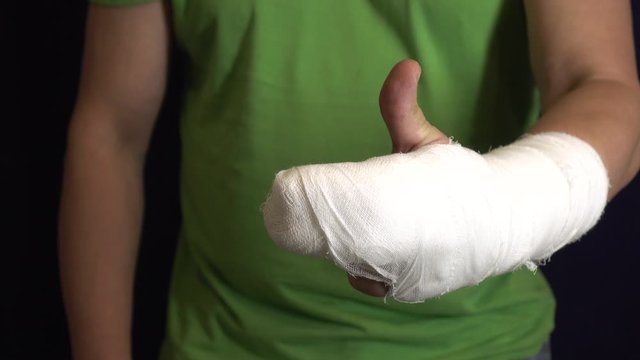The man with the arm in a cast shows that everything is in order . Man's hand in bandages after surgery.
