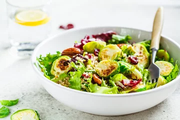 Rollo Gebratener Rosenkohlsalat mit Quinoa, Preiselbeeren und Nüssen in weißer Schüssel. Gesundes veganes Lebensmittelkonzept. © vaaseenaa