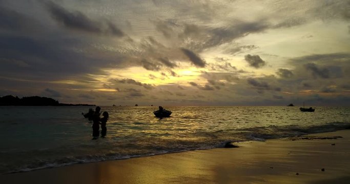 Silhouette of hugging couple standing on shallow waters near fishing boats shore on a romantic sunset in Didicas, Philippines