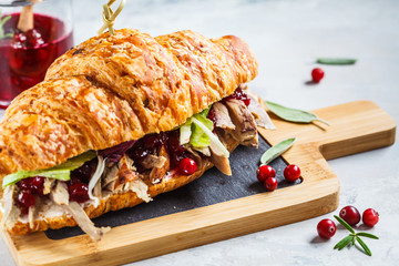 Croissant sandwich with duck meat, cream cheese and cranberry sauce on the board.
