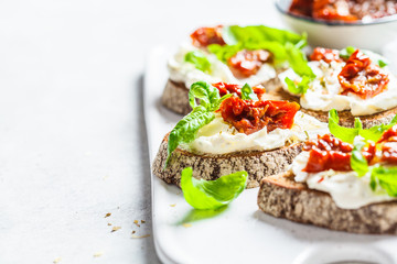 Sandwiches with cottage cheese and sun-dried tomatoes on white board.