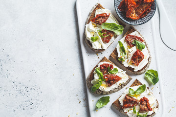 Sandwiches with cottage cheese and sun-dried tomatoes on white board, top view.