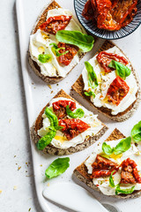 Sandwiches with cottage cheese and sun-dried tomatoes on white board, top view.
