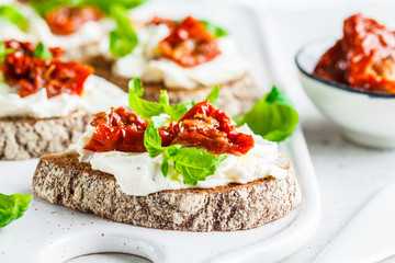 Sandwiches with cottage cheese and sun-dried tomatoes on white board.