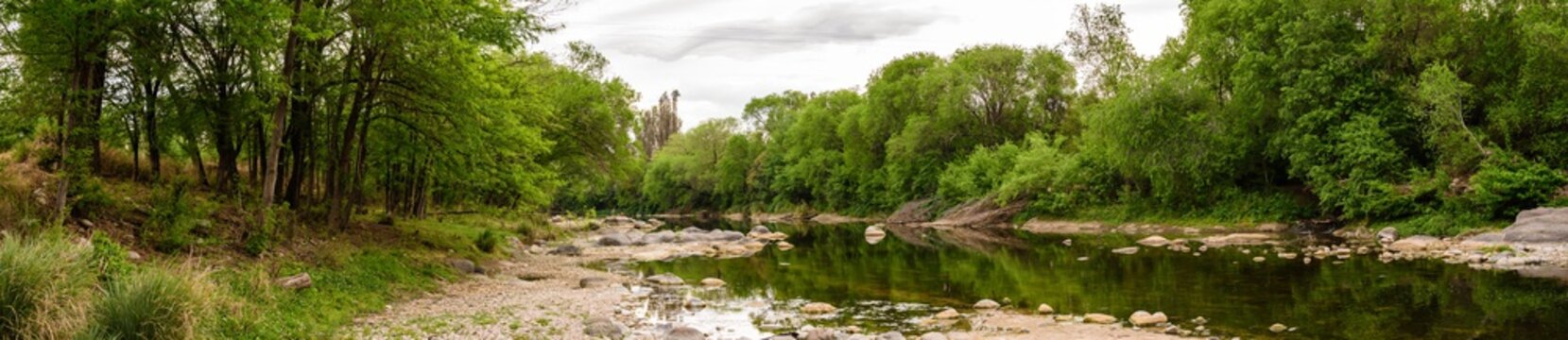 Río serrano con arboleda y bosque en un día nublado de primavera. Paisaje panorámico. Ecosistema serrano