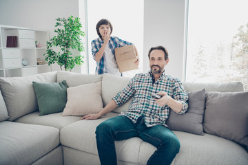 Portrait of two nice attractive cheerful cheery guys pre-teen son prepared secret carton box for dad's day birthday occasion daddy watching tv in light white modern interior house living-room