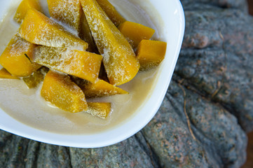 Yummy pumpkin and sweet coconut milk in white bowl, popular Thai dessert on top of ripe fresh Thai pumpkin background.