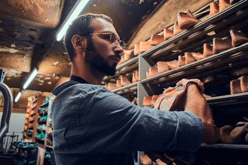 Focused bearded cobbler is looking for right shoe form at the storage.
