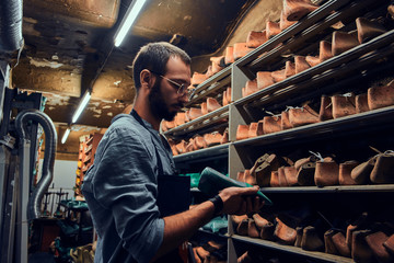 Young shoemaker is searching for special shoe form for his new project. - obrazy, fototapety, plakaty